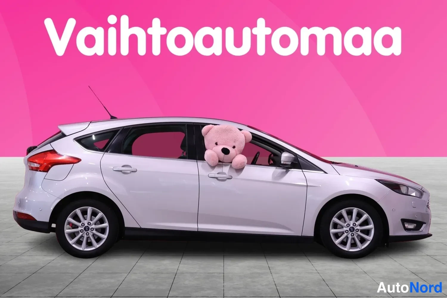 Etuviisto, nokka oikealle: Hopeanvärinen Ford Focus -viistoperä sivulta, molemmat kyljet näkyvissä, pehmolelu etuikkunassa.