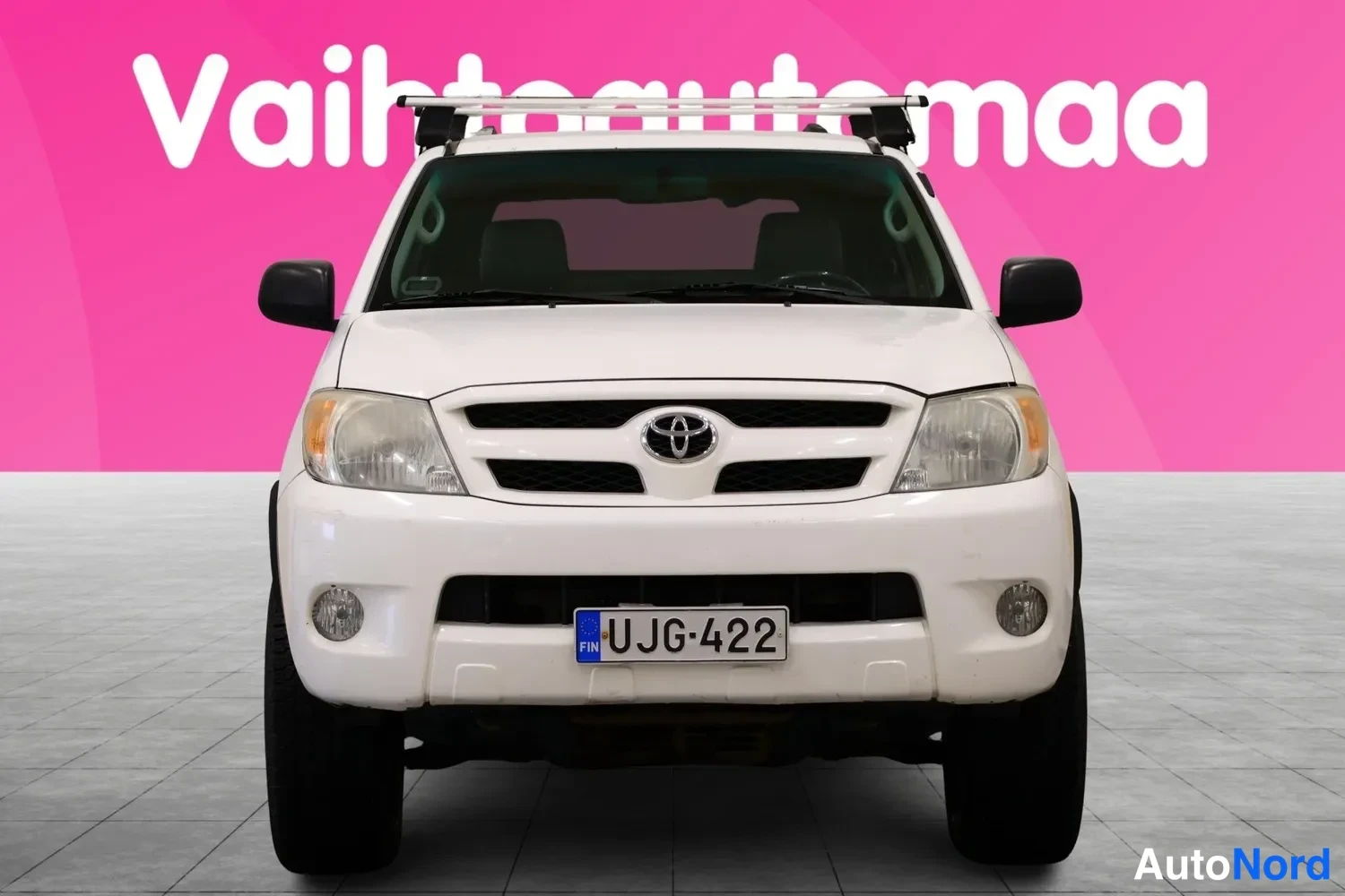 Edestä: Toyota Hilux Extra 2006 -funga suoraan edestäpäin valkoisena, kattotelineet ja rekisterikilpi näkyvissä.