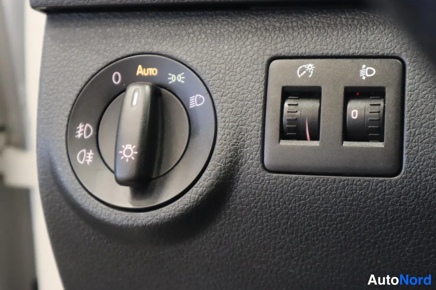 Yksityiskohta: Auton kojelaudan valokytkin, jossa Auto-asetus, sekä sumuvalojen ja valonsäätimen nappeja.