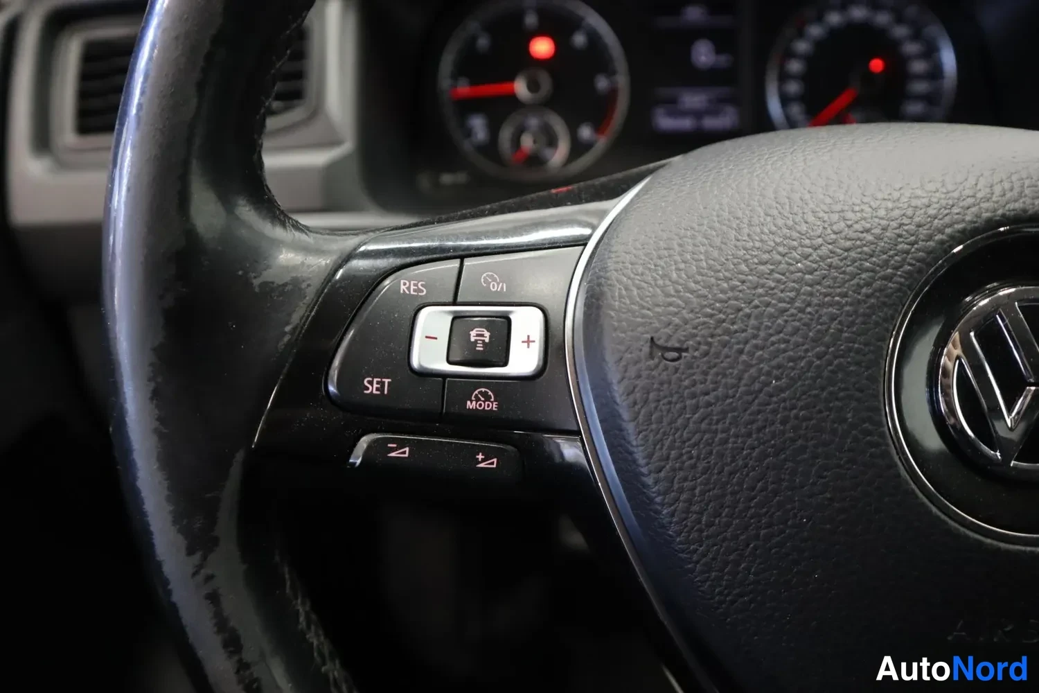 Yksityiskohta: Volkswagenin ohjauspyörä ja hallintapainikkeita, mm. RES- ja SET-napit, taustalla mittaristo.