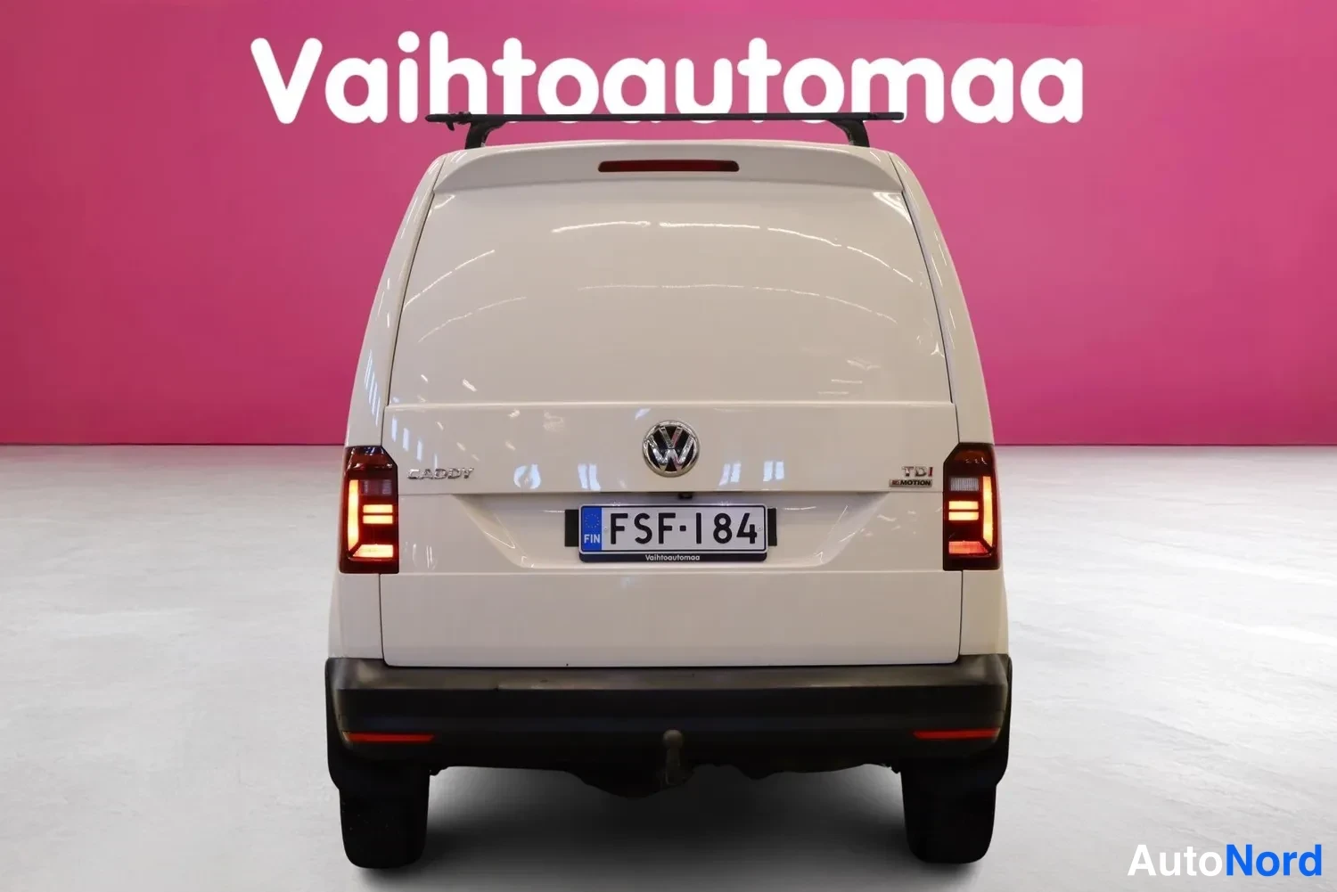 Takaa: Valkoisen pakettiauton suora takanäky, rekisteritunnus, VW-merkki ja Caddy-teksti takaluukussa.