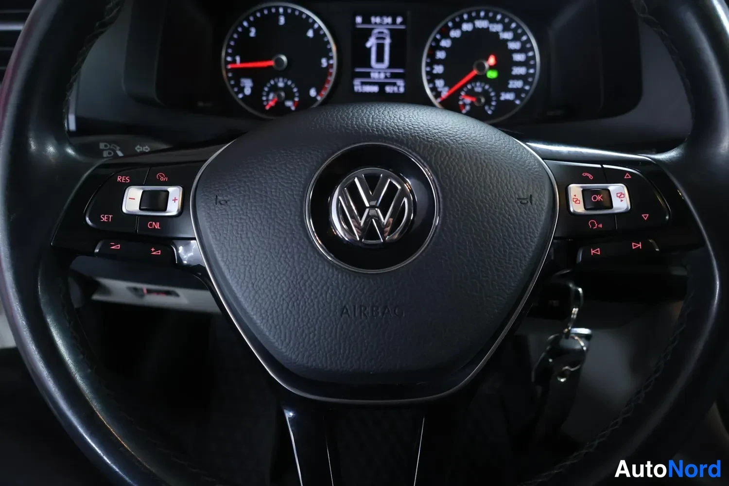 Muu: VW-merkillinen ohjauspyörä, jossa monitoiminappulat (RES, SET, CNL, OK) ja AIRBAG-teksti. Taustalla mittaristo ja avain lukossa.