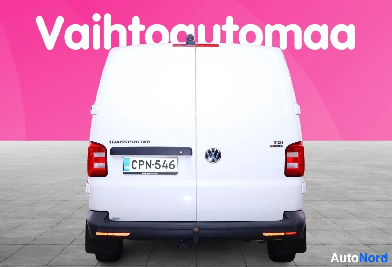 Takaa: Valkoinen pakettiauto suoraan takaa, takaluukilla merkinnät Transporter ja TDI.