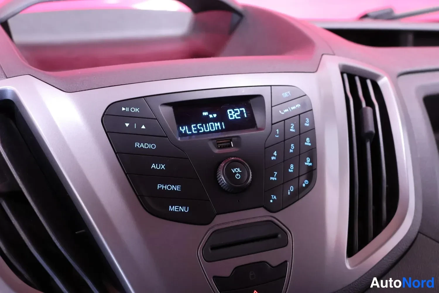Yksityiskohta: Ford Transitin kojelaudan radio- ja puhelinpainikkeet, näytössä kanava 82,7 ja teksti YLE SUOMI.