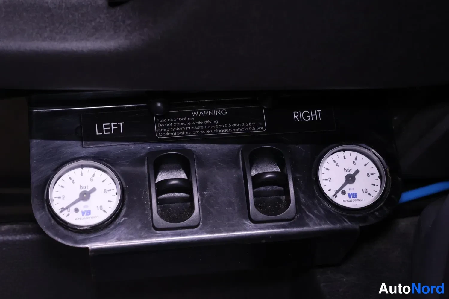 Yksityiskohta: VB Airsuspension ilmajousituksen paineenvalvontapaneeli: LEFT- ja RIGHT-merkityt painemittarit, kytkimet ja varoitustarra.