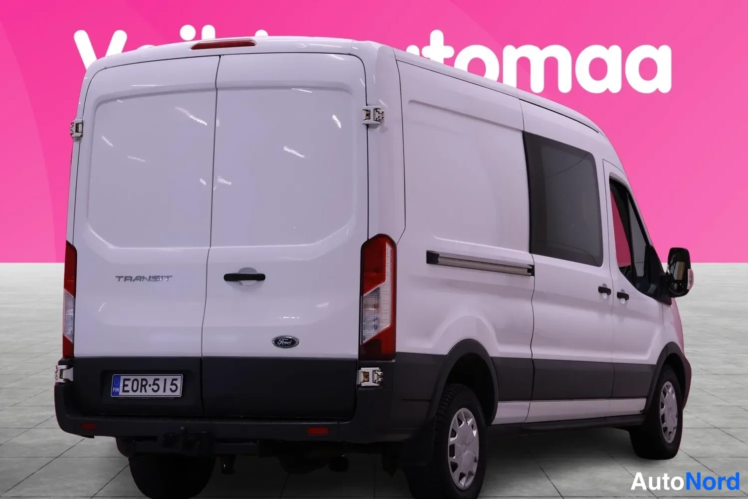Takaviisto: Valkoinen Ford Transit -pakettiauto takaviistöstä oikealta, Transit-teksti takapaneelissa, rekisterikilpi.