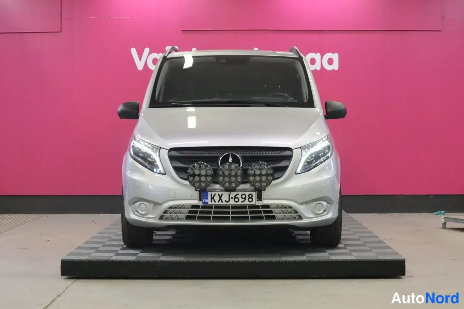 Edestä: Hopeinen pakettiauto suoraan edestä kuvattuna, lisävaloja keulassa ja rekisteritunnus.