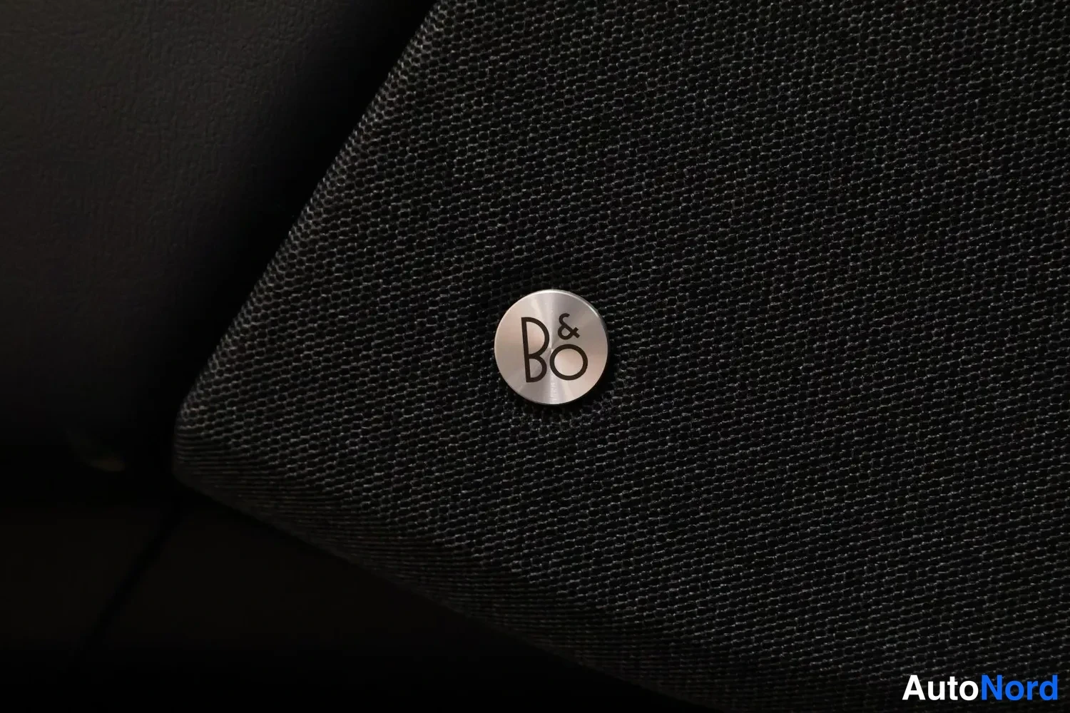 Edestä: Musta kaiutinkangas ja B&O (Bang & Olufsen) -logomerkki kaiuttimen etupaneelissa.