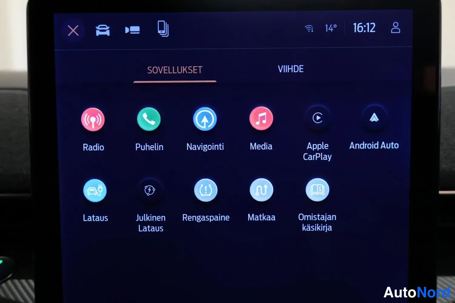 Edestä: Infotainment-järjestelmän SOVELLUKSET-valikko, jossa kuvakkeet Radio, Puhelin, Navigointi, Media, Apple CarPlay, Android Auto, Lataus, Julkinen Lataus, Rengaspa