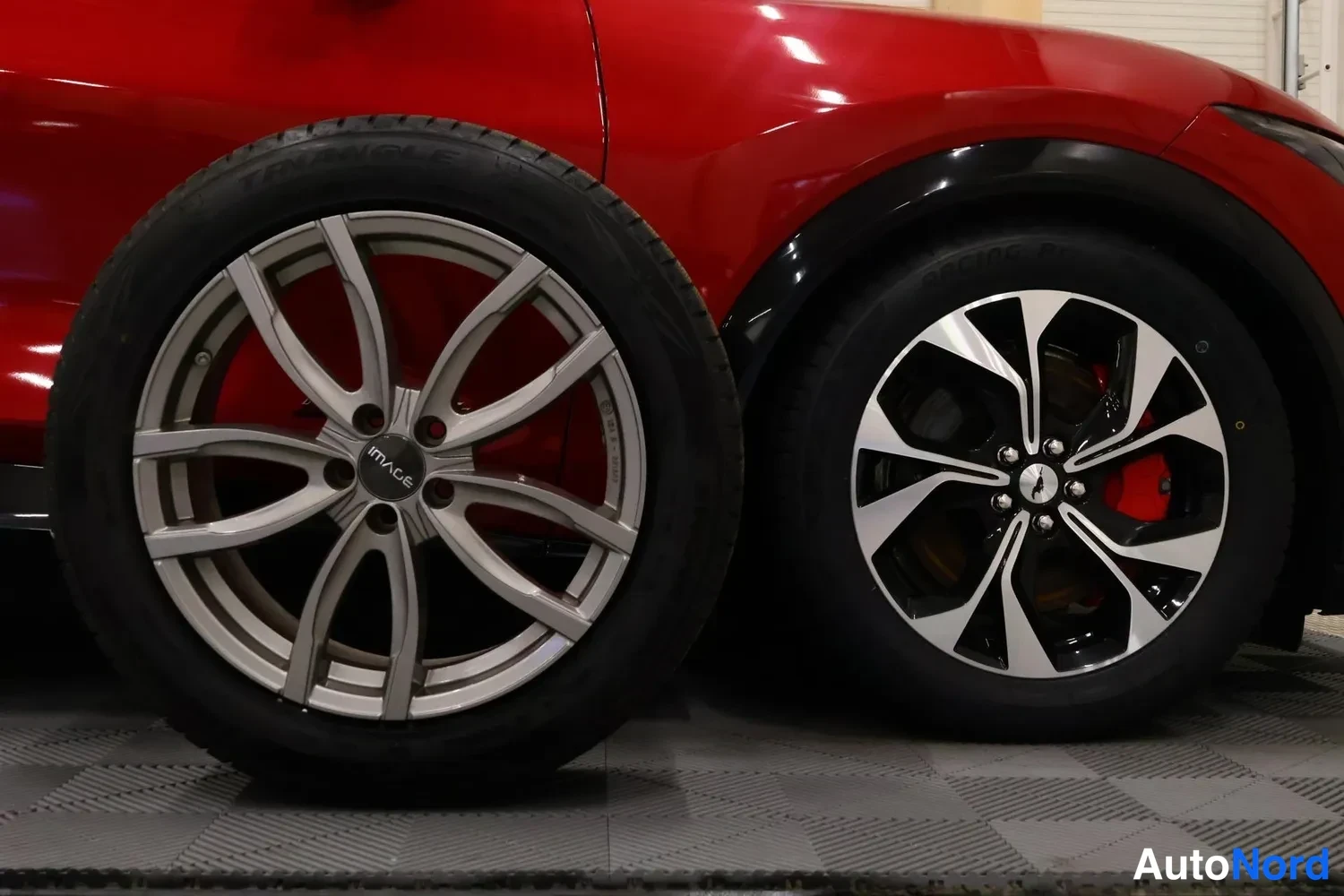 Muu: Punainen auto, jonka takapyörä ja vieressä oleva hopeavanteinen varapyörä kuvattuna sisätiloissa.