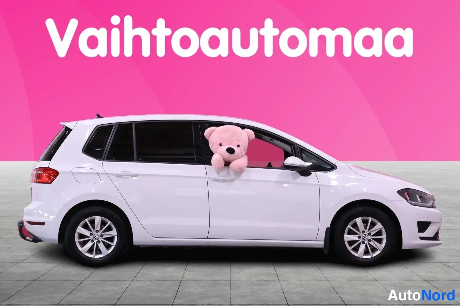 Sivulta: Valkoinen Volkswagen Golf Sportsvan sivulta vasemman laidan suunnasta, pehmolelu takapenkin ikkunassa.