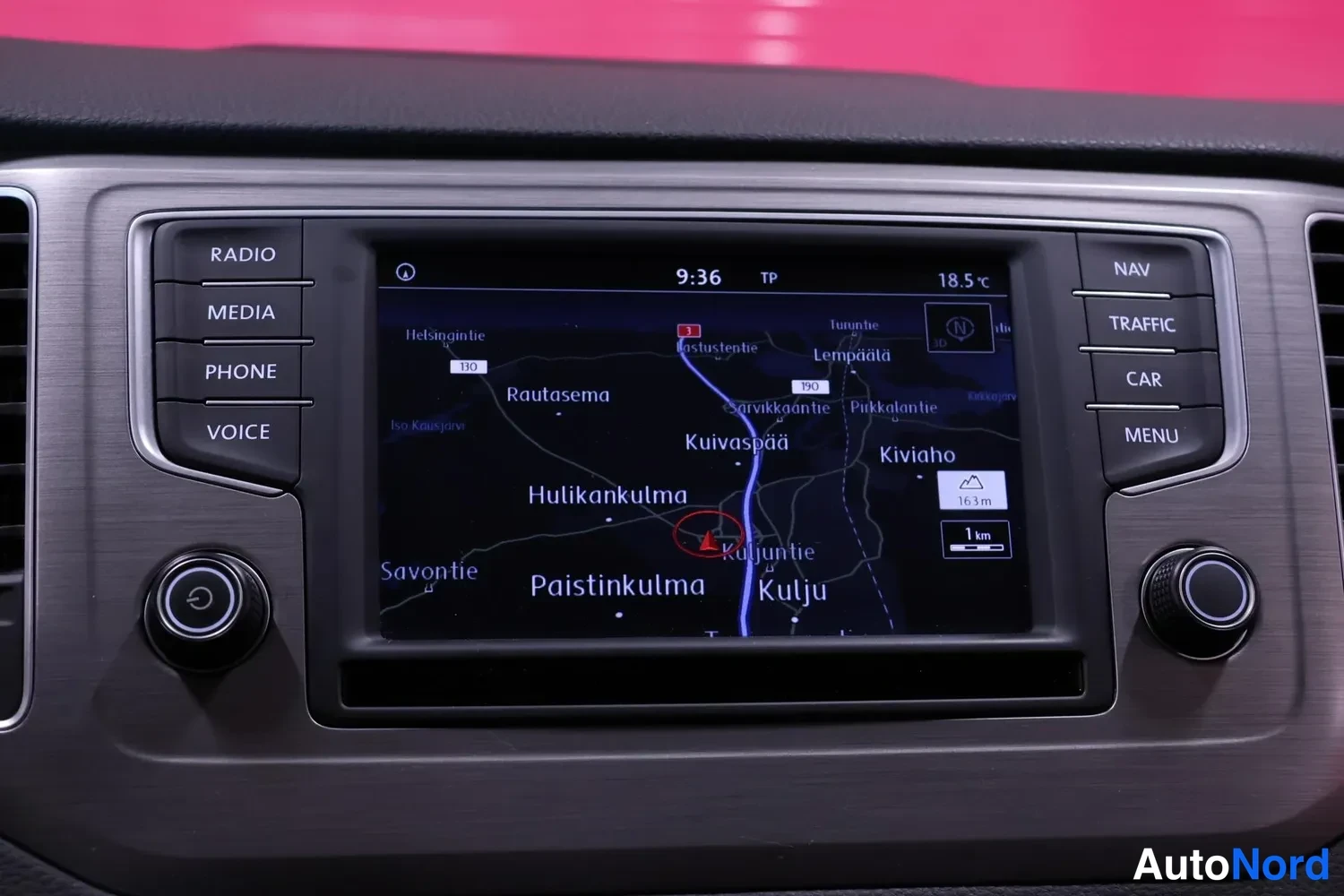 Sivulta: Kojetaulun infotainment-näyttö näyttää navigointikartan paikkatiedoilla; nappien R ja C tunnisteet ja ääniohjausnappi näkyvät.