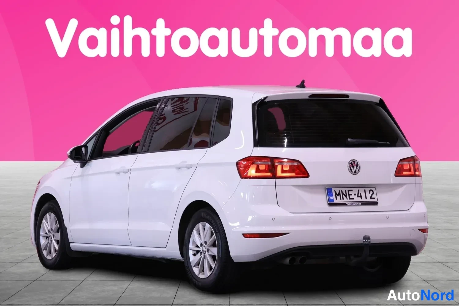 Takaviisto: Valkoisen farmarimallisen henkilöauton takaosa ja vasen kylki; takavaloissa palaa hehkuvat osiot, rekisterikilpi ja tunniste on VW-embleema takaluukissa.