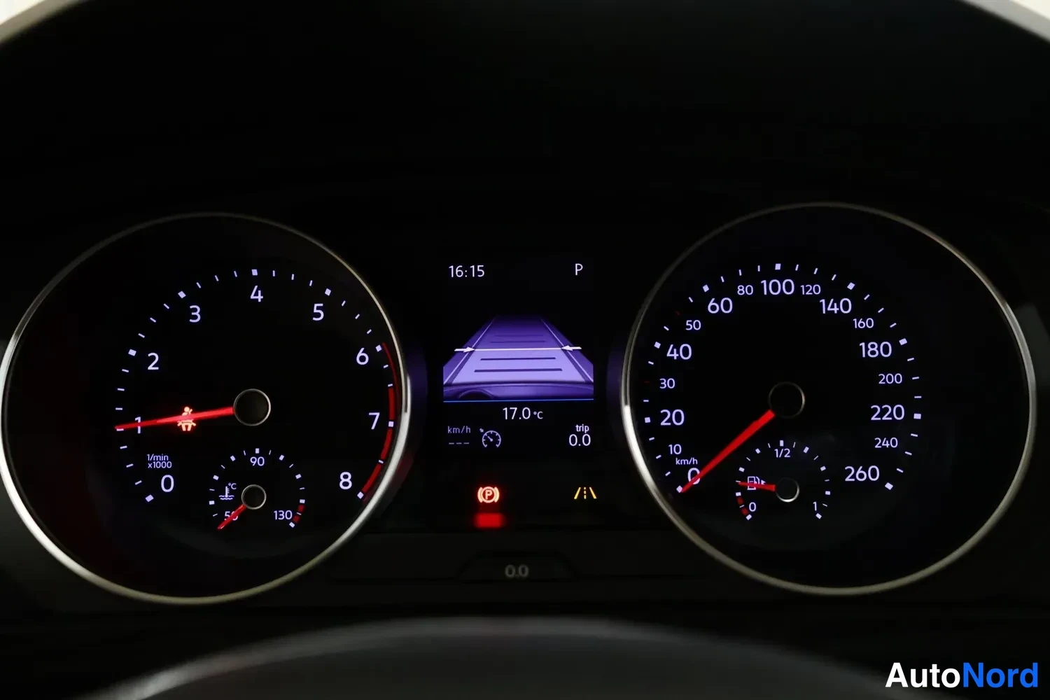 Yksityiskohta: Hyvin valaistu mittaristo pimeässä sisätilassa: kierroslukumittari ja nopeusmittari 0–260 km/h, keskellä näyttö, jossa pysäköintiavustajan kaavio, kello 16:15,