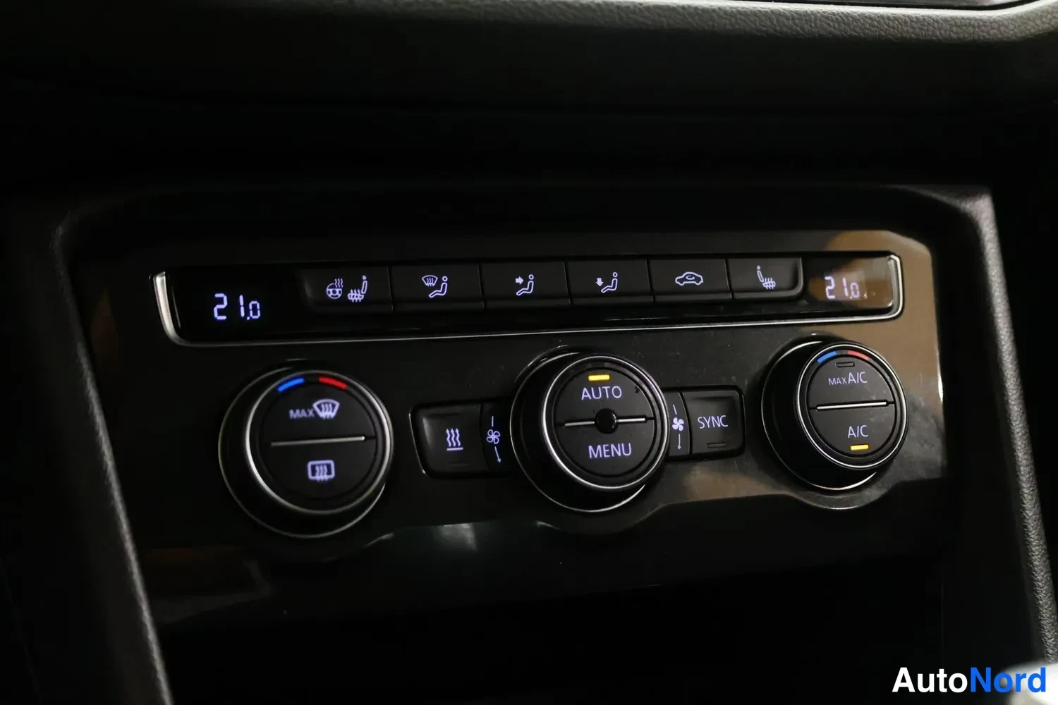 Yksityiskohta: Auton ilmastointilaitteen keskusrivi: näytöissä lämpötila 21,0, napit AUTO, MENU, SYNC, MAX A/C ja A/C sekä lämmitys- ja ilmanohjauksen painikkeet.