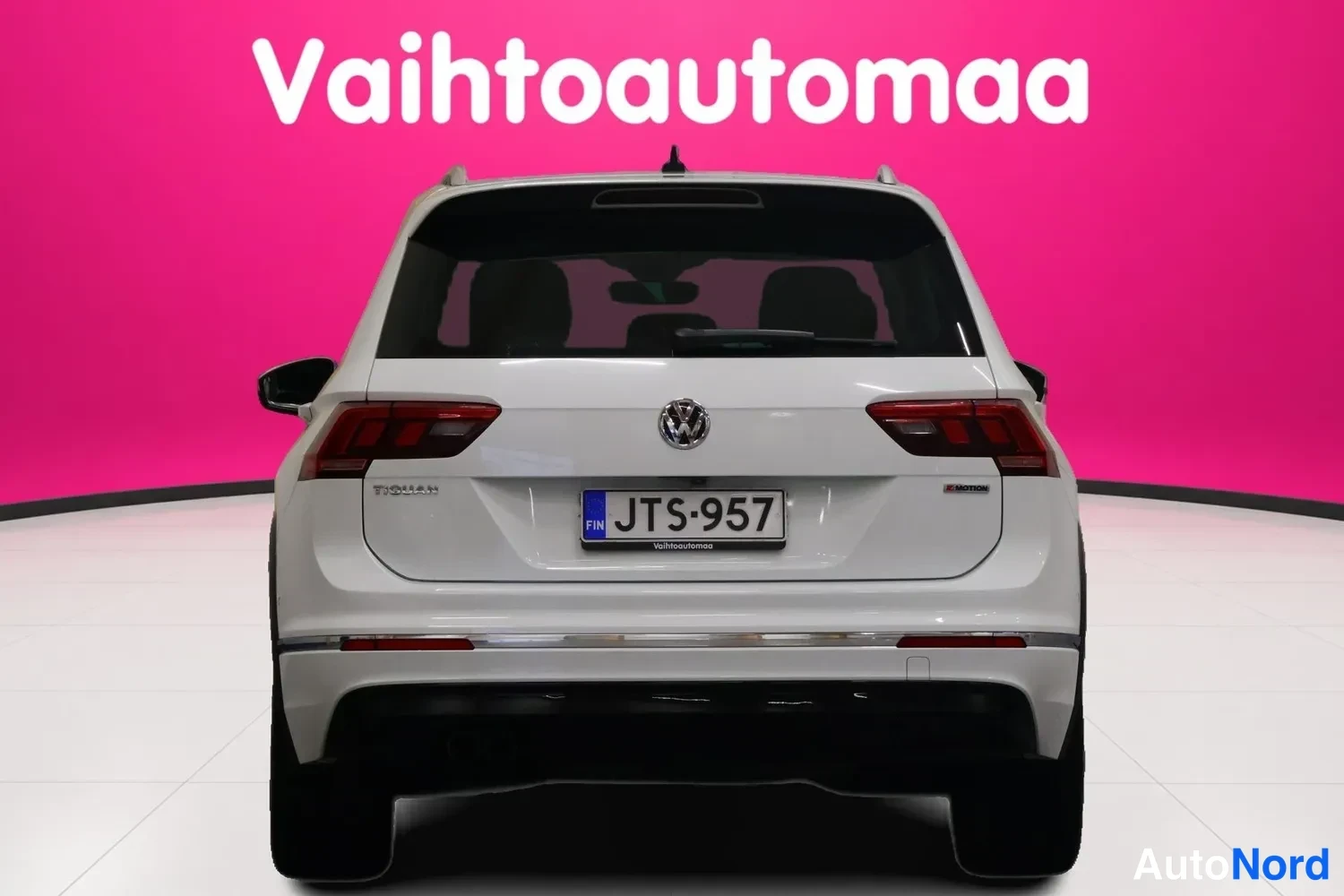 Takaa: Auton takanäkyvyys suoraan takaa: valkoinen Volkswagen Tiguan, Volkswagen-emblem, takavalot, rekisterikilpi ja kattoantenni.