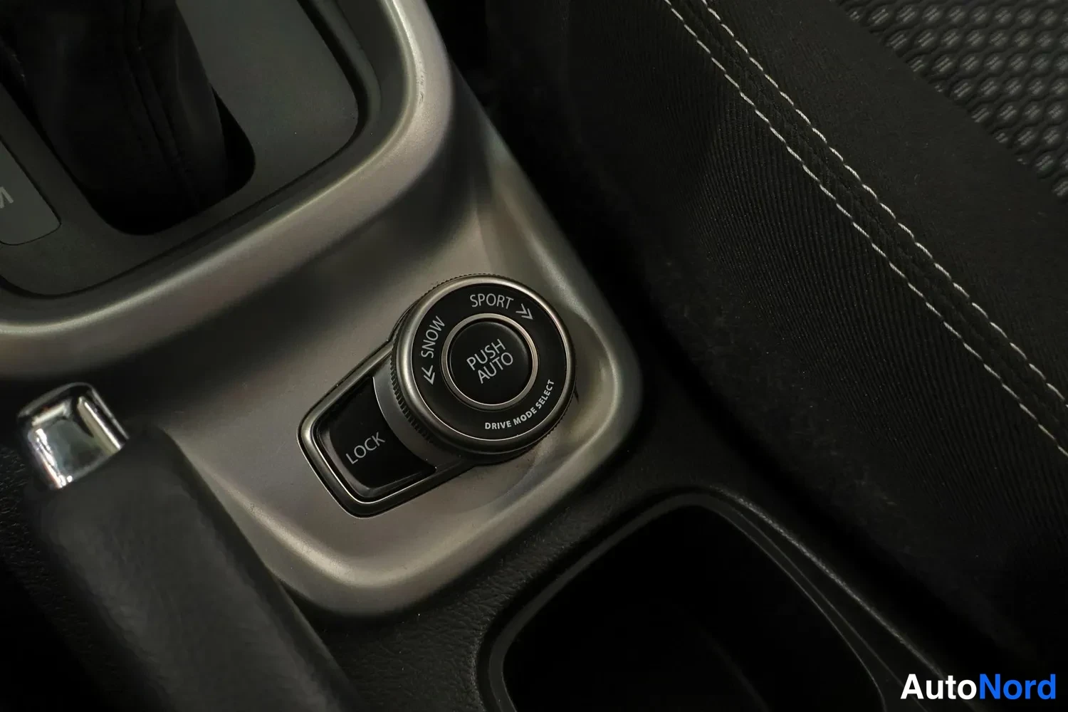 Yksityiskohta: Ajomoodin valitsinpyörä merkinnöillä SNOW, SPORT, LOCK ja PUSH AUTO, teksti DRIVE MODE SELECT.