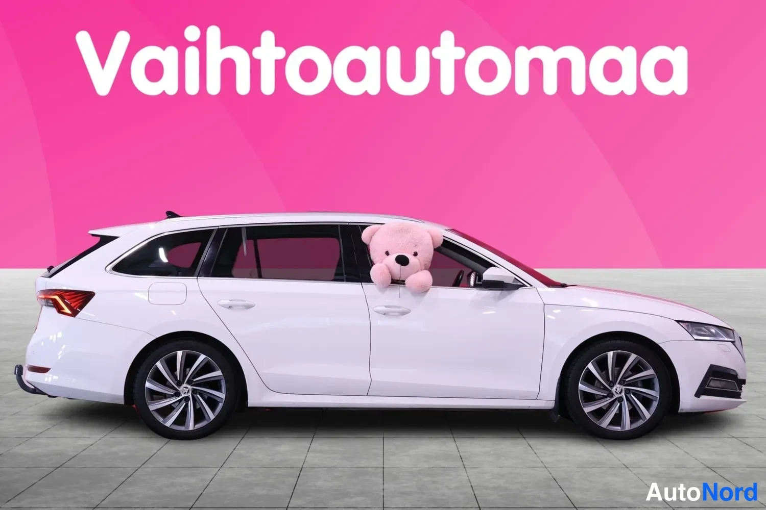 Sivulta: Valkoinen farmariauto sivulta kuvattuna, pehmolelu ikkunasta pilkottamassa.
