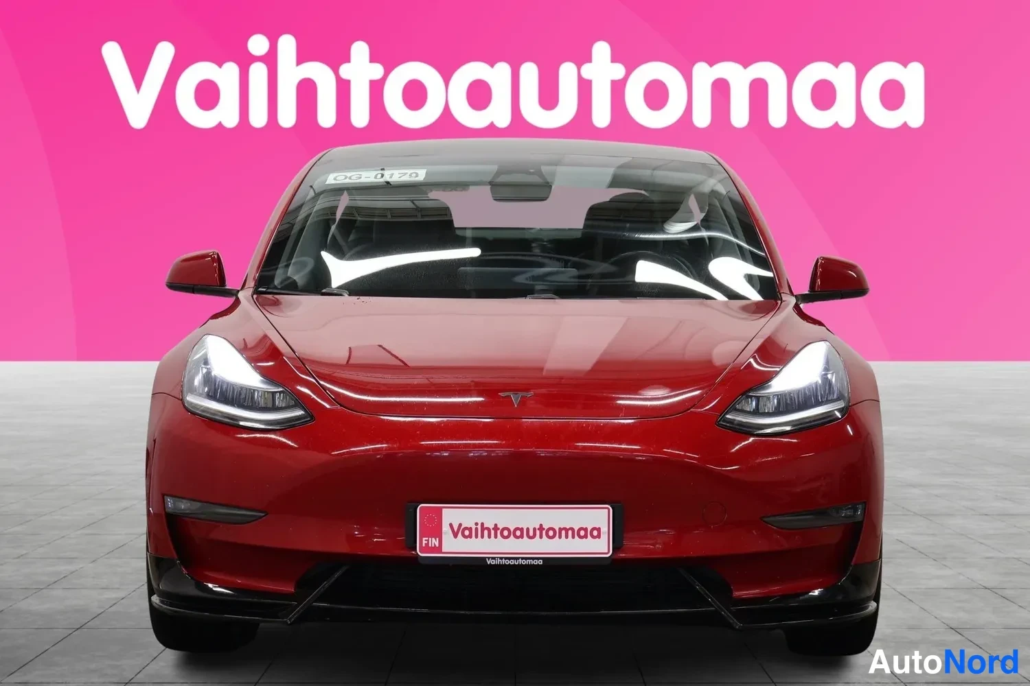 Edestä: Punainen sedan suoraan edestä kuvattuna, tumma tuulilasi ja Vaihtoautomaa-kyltti puskurissa.
