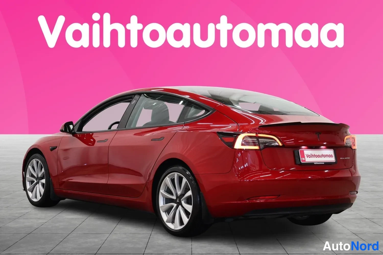 Takaviisto: Punaisen Tesla Model 3:n takaosa ja oikea sivu kuvattuna kolmannesvinkkelistä oikealta taakse.