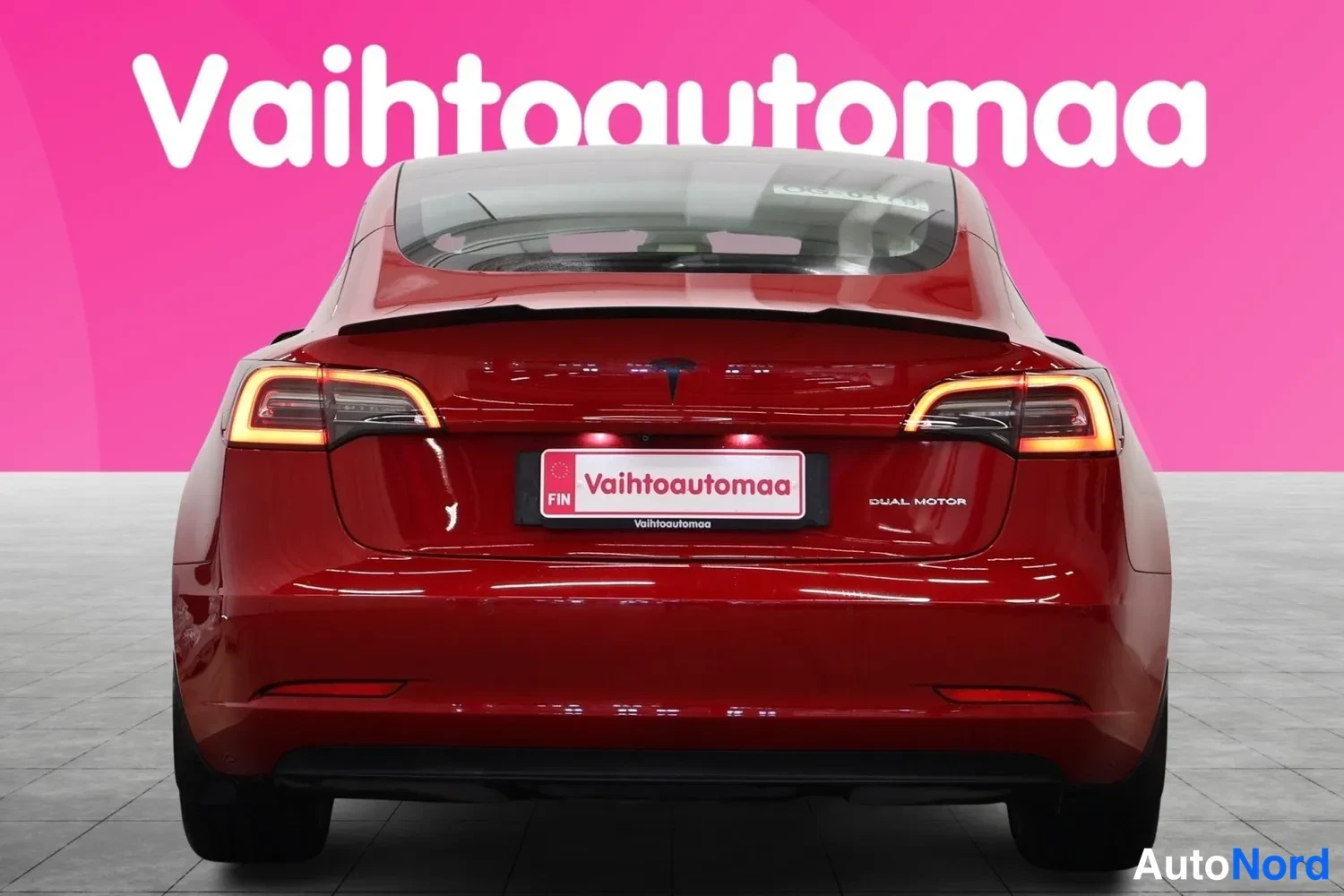 Takaa: Punaisen Tesla Model 3:n takaosa suoraan takaa, takavalot ja DUAL MOTOR -teksti näkyvissä.