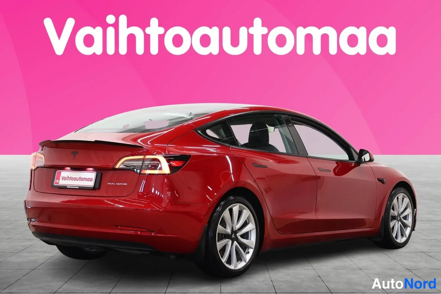 Takaviisto: Punaisen Tesla Model 3:n takaosa ja vasen sivu kuvattuna kolmannesvinkkelistä vasemmalta taakse.