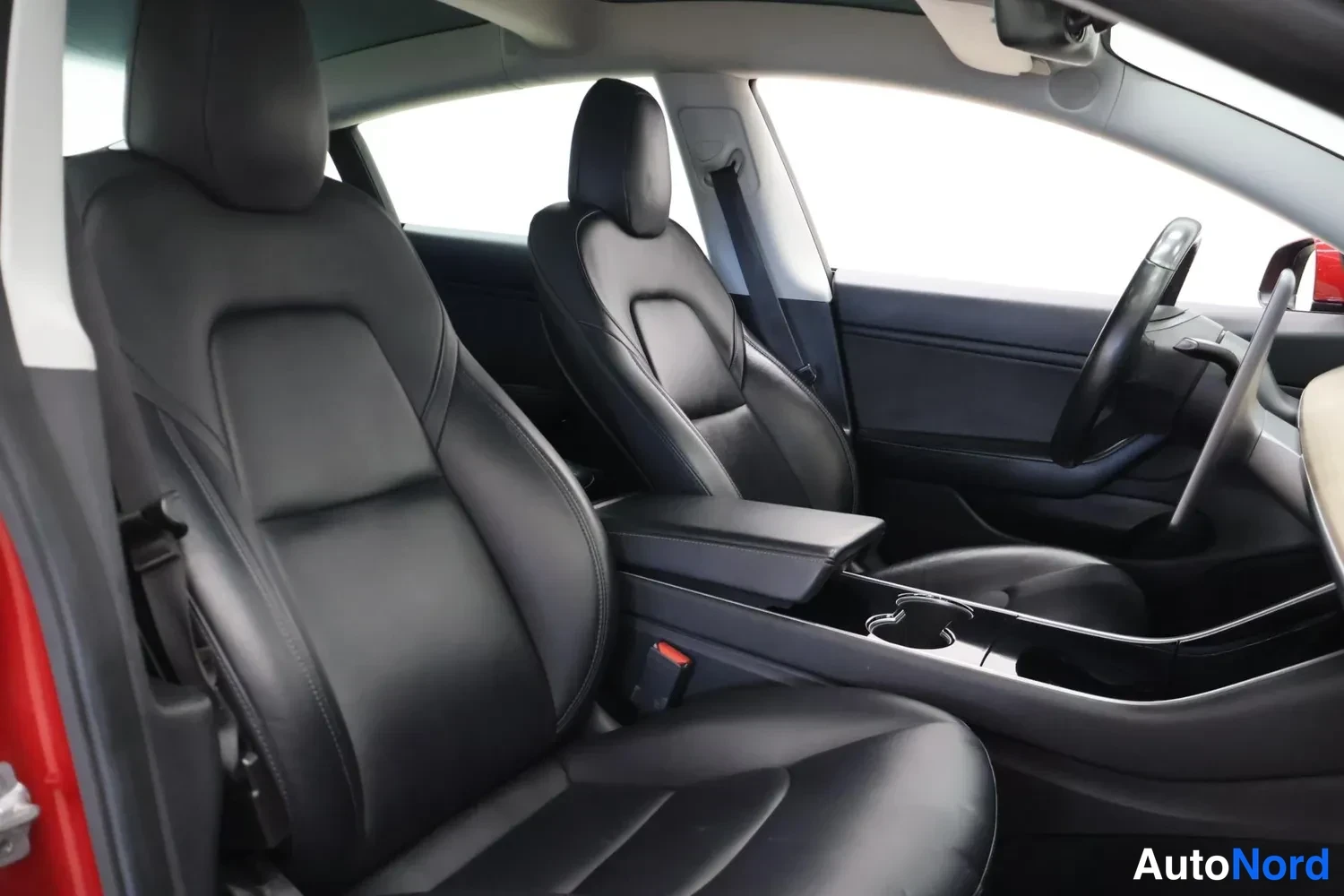 Sivulta: Tesla Model 3:n sisätilat: mustat etuistuimet, keskikonsoli ja ohjauspyörä.