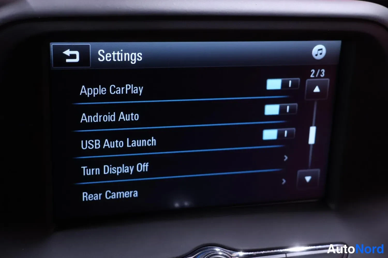 Yksityiskohta: Infotainment-järjestelmän asetusnäkymä, jossa Apple CarPlay, Android Auto ja USB Auto Launch ovat päällä; valikossa myös kohdat Turn Display Off ja Rear Camera.