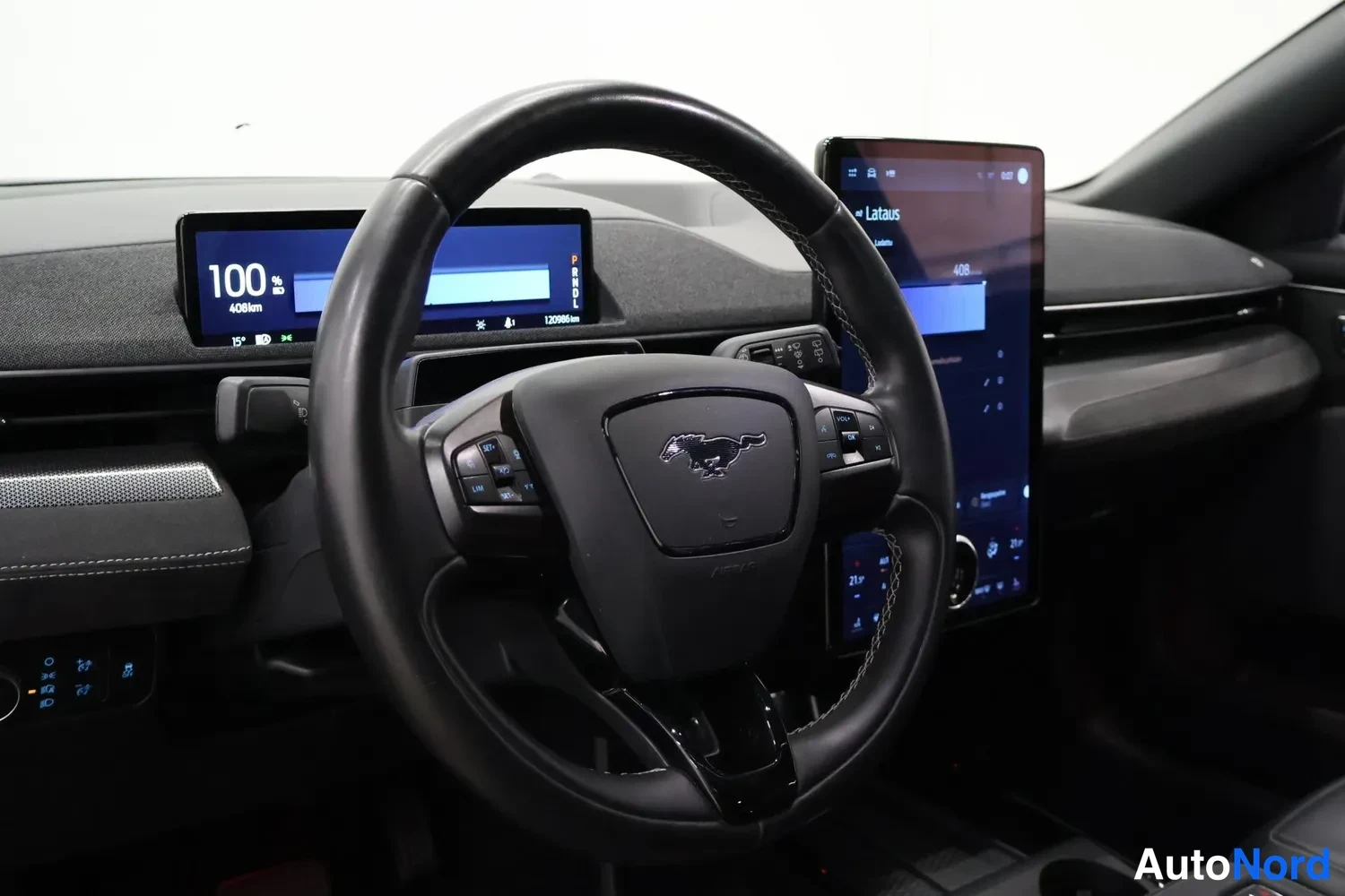 Muu: Kuljettajan näkymä kojelautaan: Mustang-ohjauspyörä, digitaalinäyttö ajotietoina (100 %, 408 km) ja keskikonsolin suuri kosketusnäyttö, jossa lukee 'Lataus'.