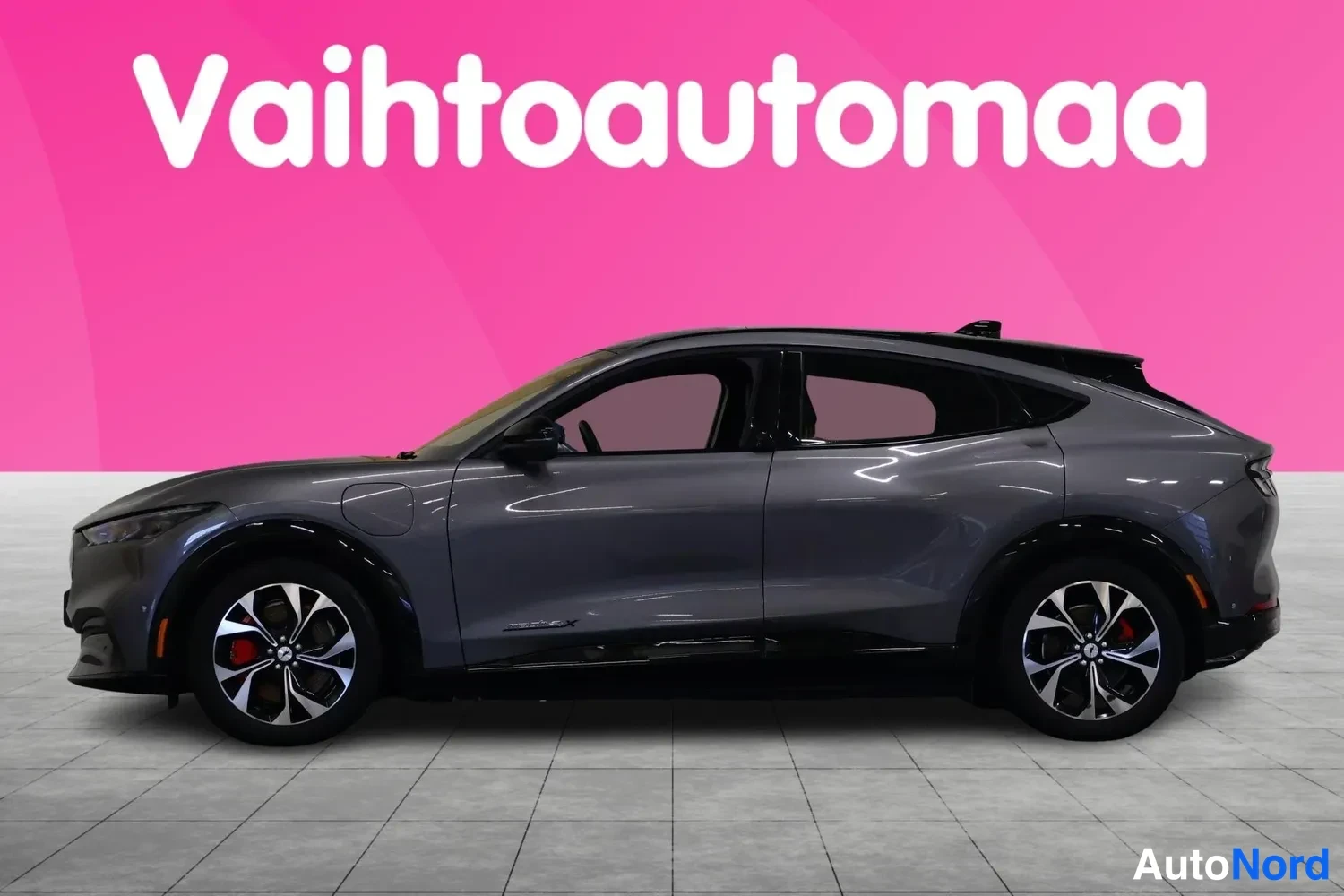 Sivulta: Tummanharmaan Ford Mustang Mach-E:n sivukuva vasemmalta, musta lasikatto ja kevytmetallivanteet.