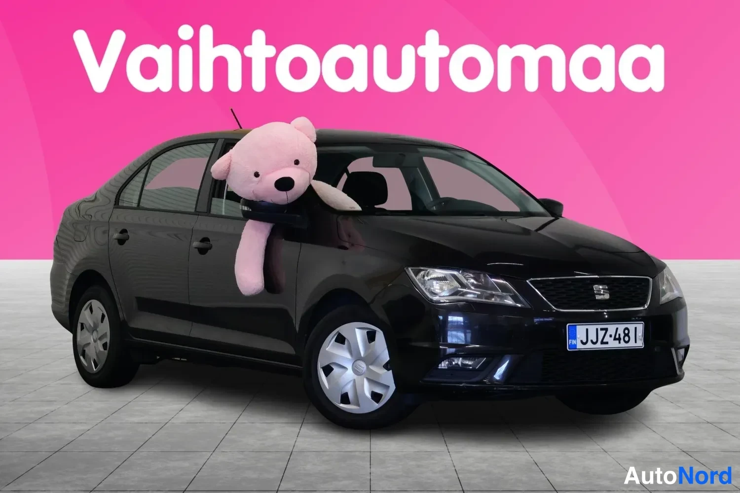 Etuviisto, nokka oikealle: Musta Seat Toledo etuokolokuvassa, nenä oikealle, suuri vaaleanpunainen pehmojätkä nojaa tuulilasiin, rekisteri.