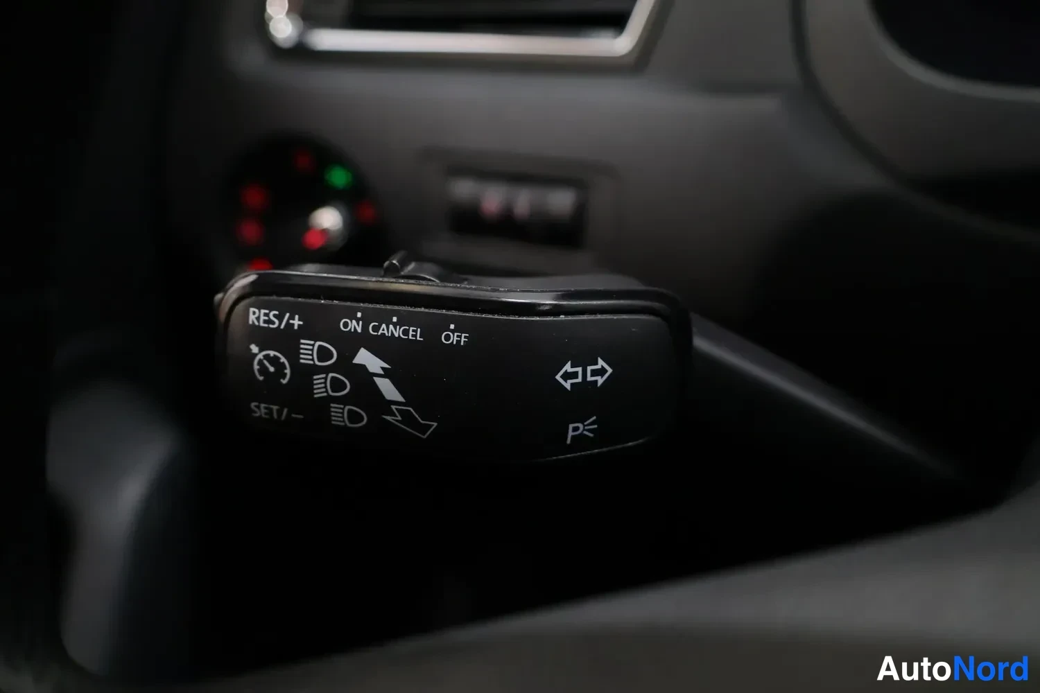 Yksityiskohta: Lähikuva ohjauspyörän oikeanpuoleisesta ohjasauvasta, jossa näkyvät Cruise Control -näppäimet RES/+, SET/-, ON/CANCEL/OFF ja viereiset merkkivalot (punainen, vi