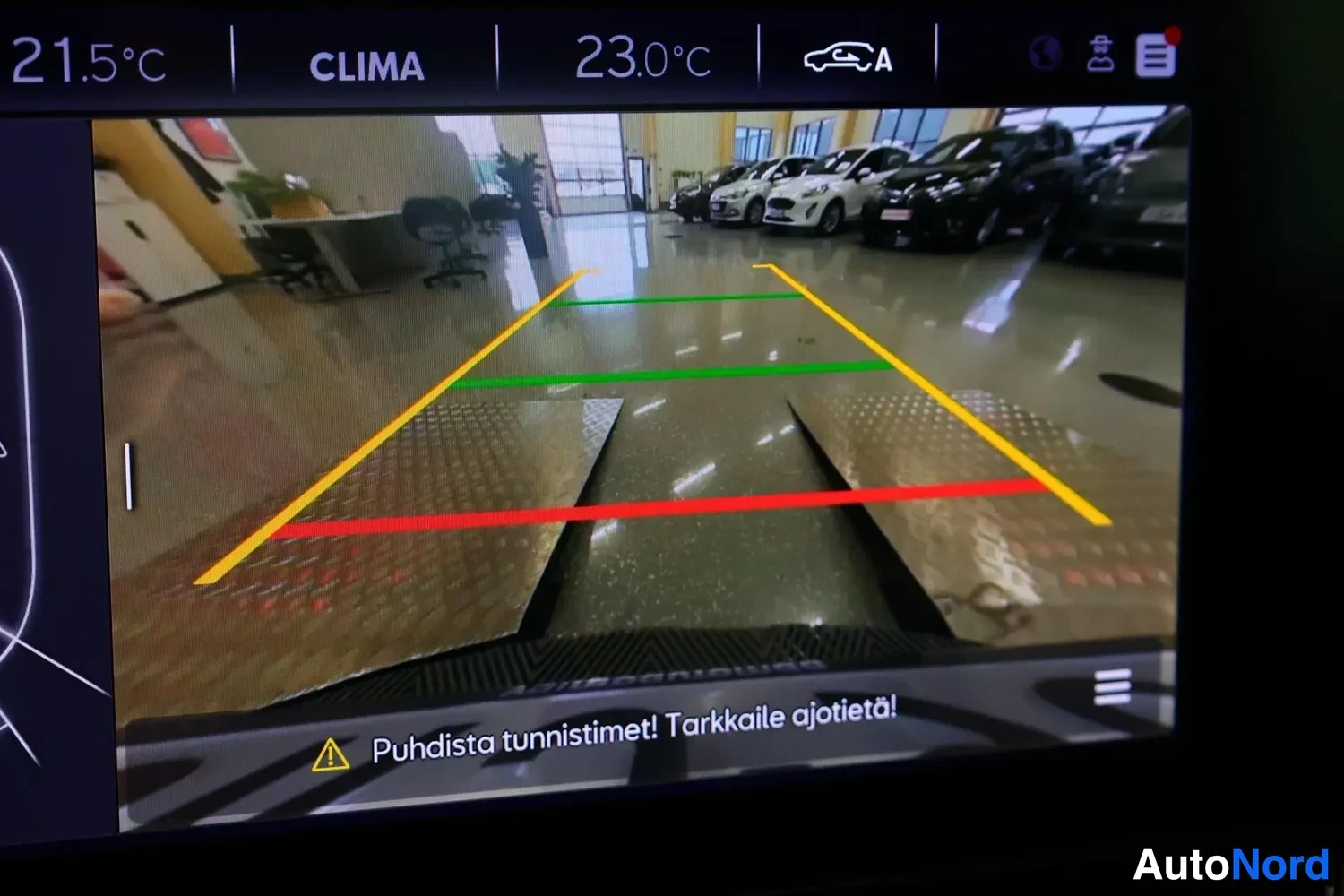 Yksityiskohta: Peruutuskameran kuva näytöllä varoituksella Puhdista tunnistimet! Tarkkaile ajetietä!