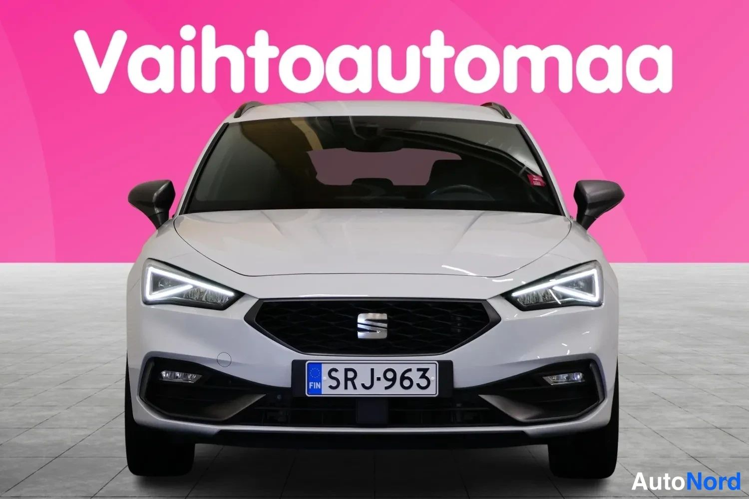 Edestä: Seat Leon Sportstourer valkoisena suoraan edestä päin, rekisteri, pinkki tausta.