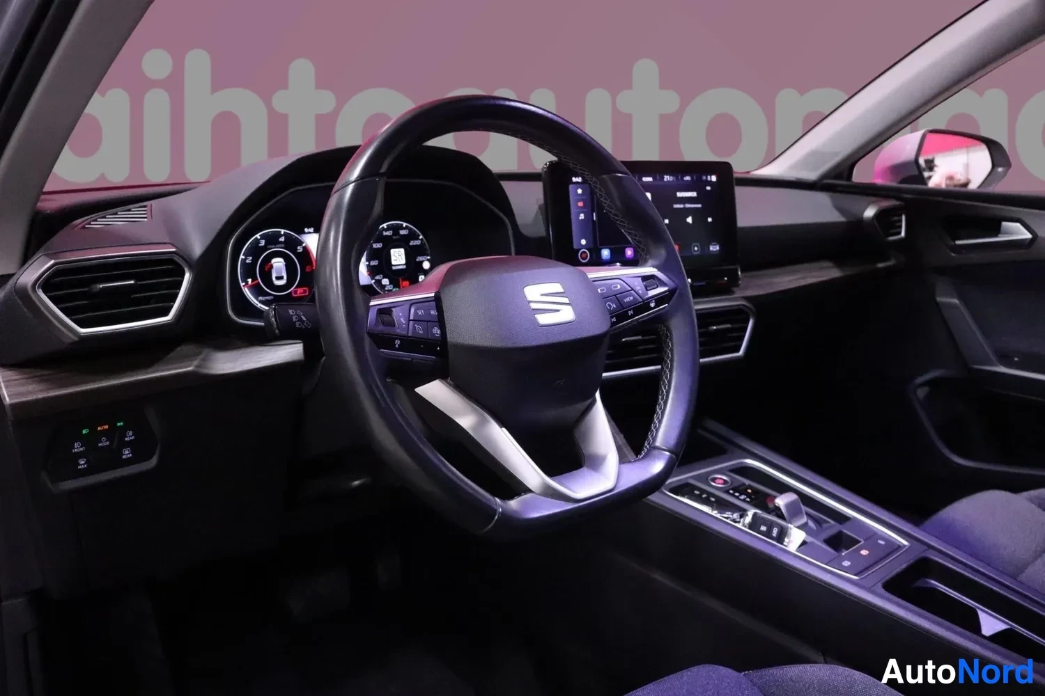 Yksityiskohta: Seat-henkilöauton ohjaamo: Seat-merkillinen ohjauspyörä, digitaalinen mittaristo ja kosketusnäytöllinen medianäyttö keskikonsolissa, tumma sisusta.