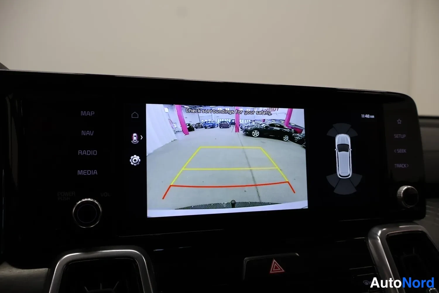Muu: Kojelaudan infotainment-näyttö näyttää peruutuskameran kuvan ohjausviivoineen ja tekstin Check surroundings for your safety.