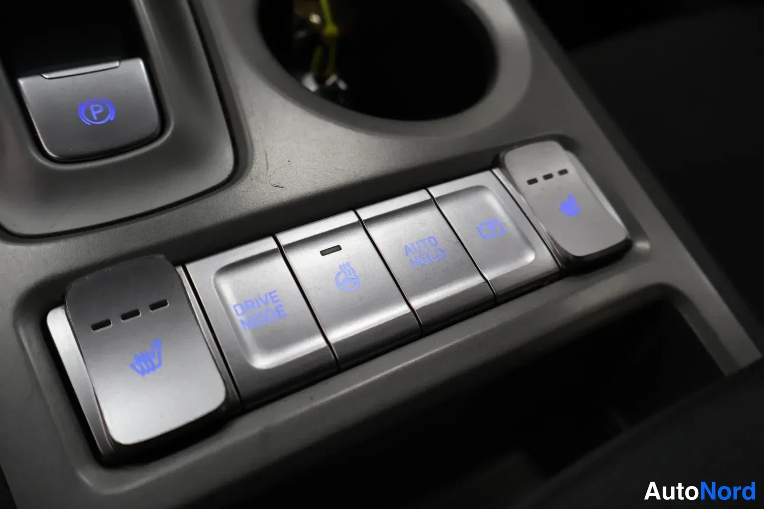 Yksityiskohta: Sisätilan lähikuva keskikonsolin painikerivistä sinisellä taustavalaistuksella: sähköinen käsijarru, DRIVE MODE, AUTO HOLD, istuimenlämmitys- ja ratinlämmityspa