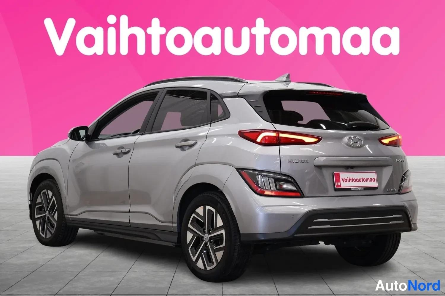 Takaviisto: Hopeanharmaa Hyundai Kona takaa sivusta vasemmalle kuvattuna, rekisteritunnus piilotettu Vaihtoautomaa-kyltillä.
