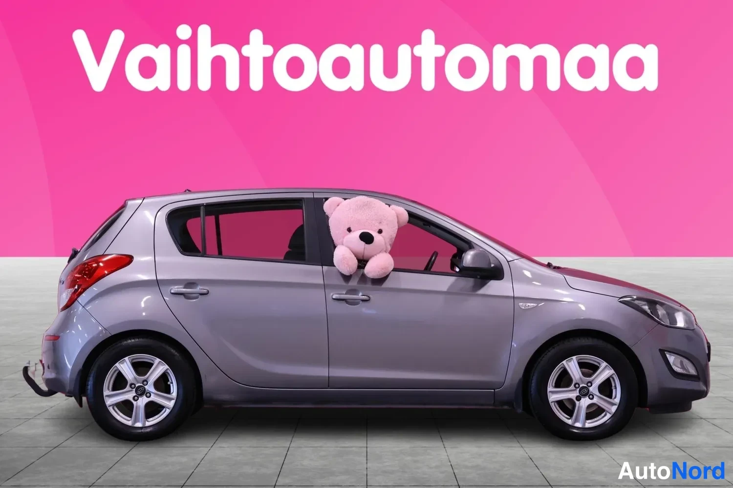 Sivulta: Hyundai i20 -henkilöauto sivulta vasemman kyljen näkymässä, vasemman etuoven ikkunasta kurkistaa vaaleanpunainen pehmolelu.