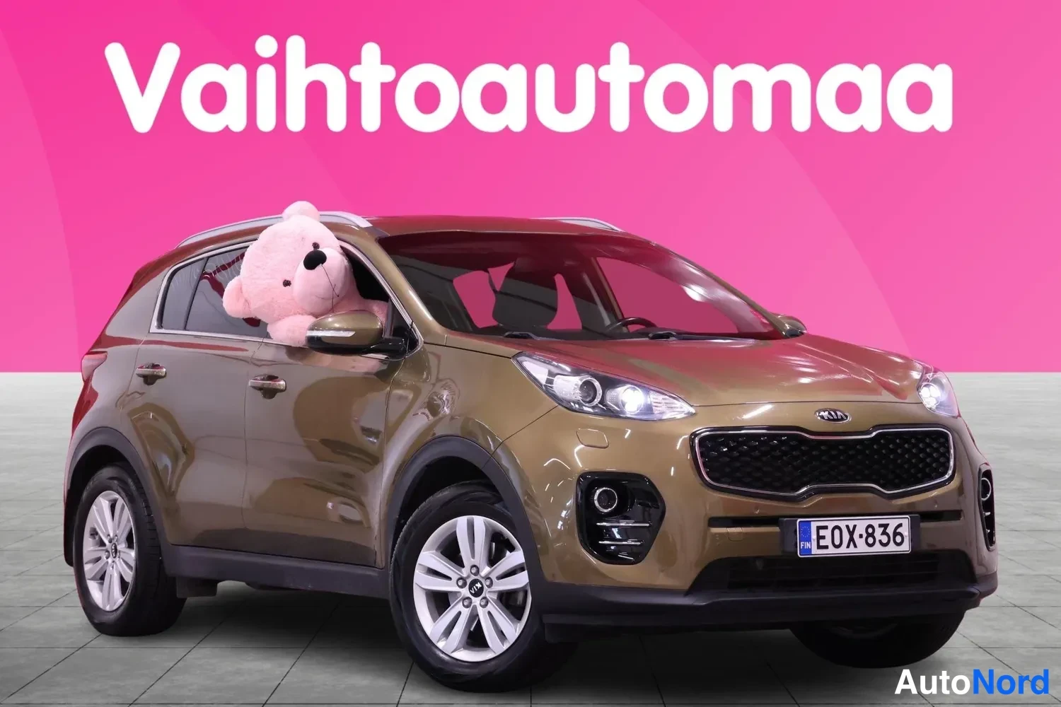 Etuviisto, nokka oikealle: Ruskean metallinhohtoinen Kia Sportage kuvattu etuviistöstä oikealta, etusäleikkö ja valot näkyvät, kilpi.