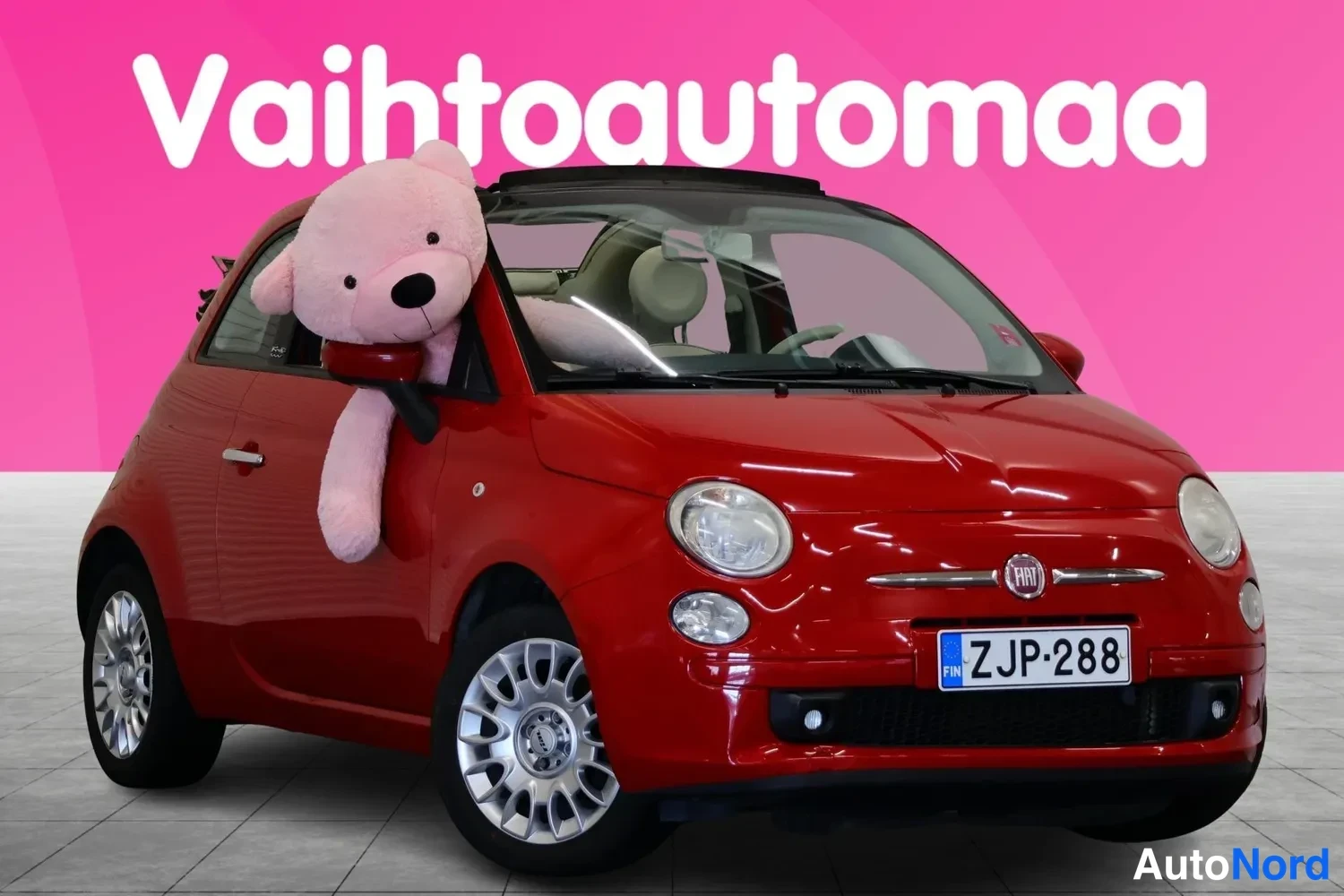 Etuviisto, nokka oikealle: Punainen Fiat 500C avokatto auki etuviistossa, rekisteritunnus, pehmo-karhu ovessa.