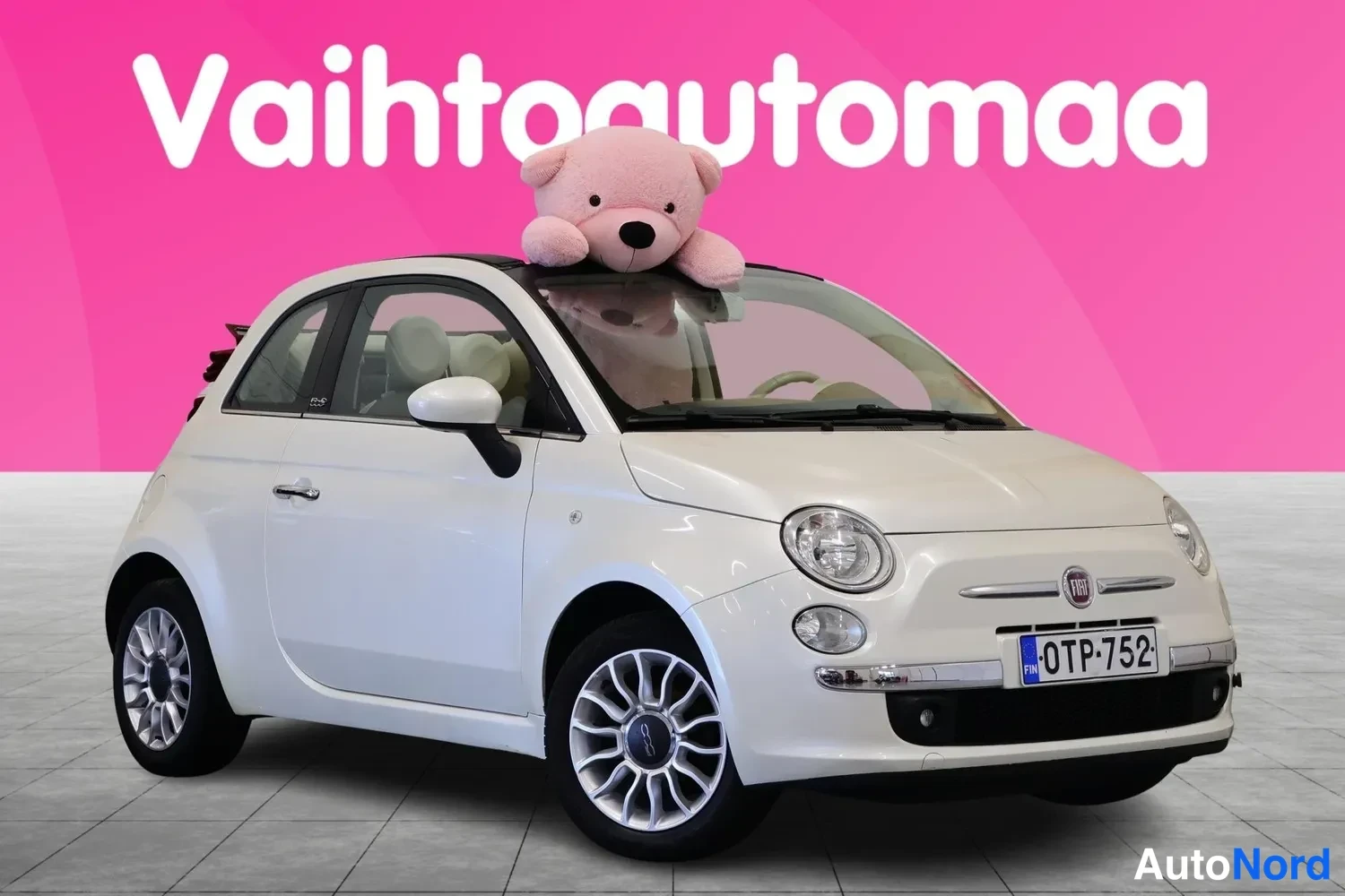 Etuviisto, nokka oikealle: Valkoinen Fiat 500C avotakaa etukulmasta oikealta, rekisteritunnus, vaaleat metallivanteet ja pinkki tausta.