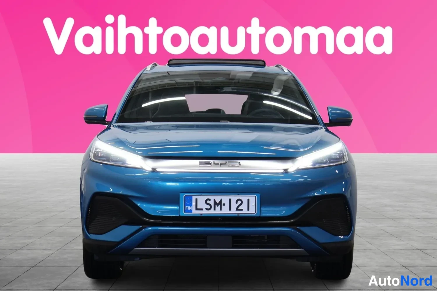 Edestä: Sininen BYD Atto 3 suoraan edestä, rekisterikilpi ja BYD-teksti konepellin reunassa.