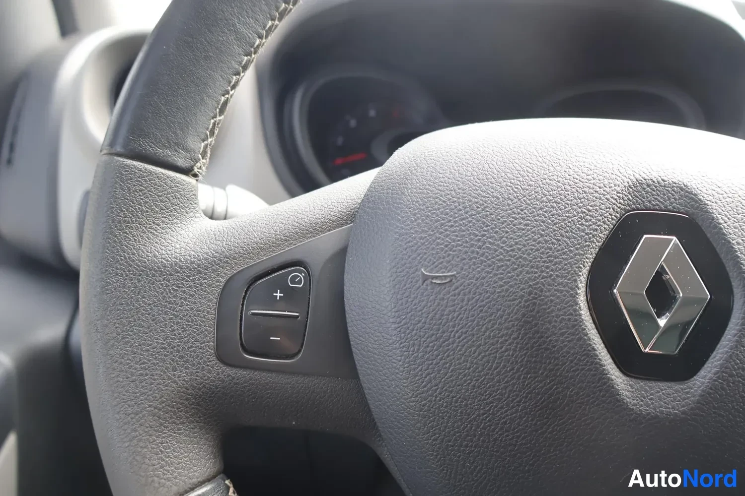 Muu: Renault-ohjauspyörän vasen puhelinpainike (+/− ja kuvake) lähikuvassa, kojelauta taustalla sumuisena.