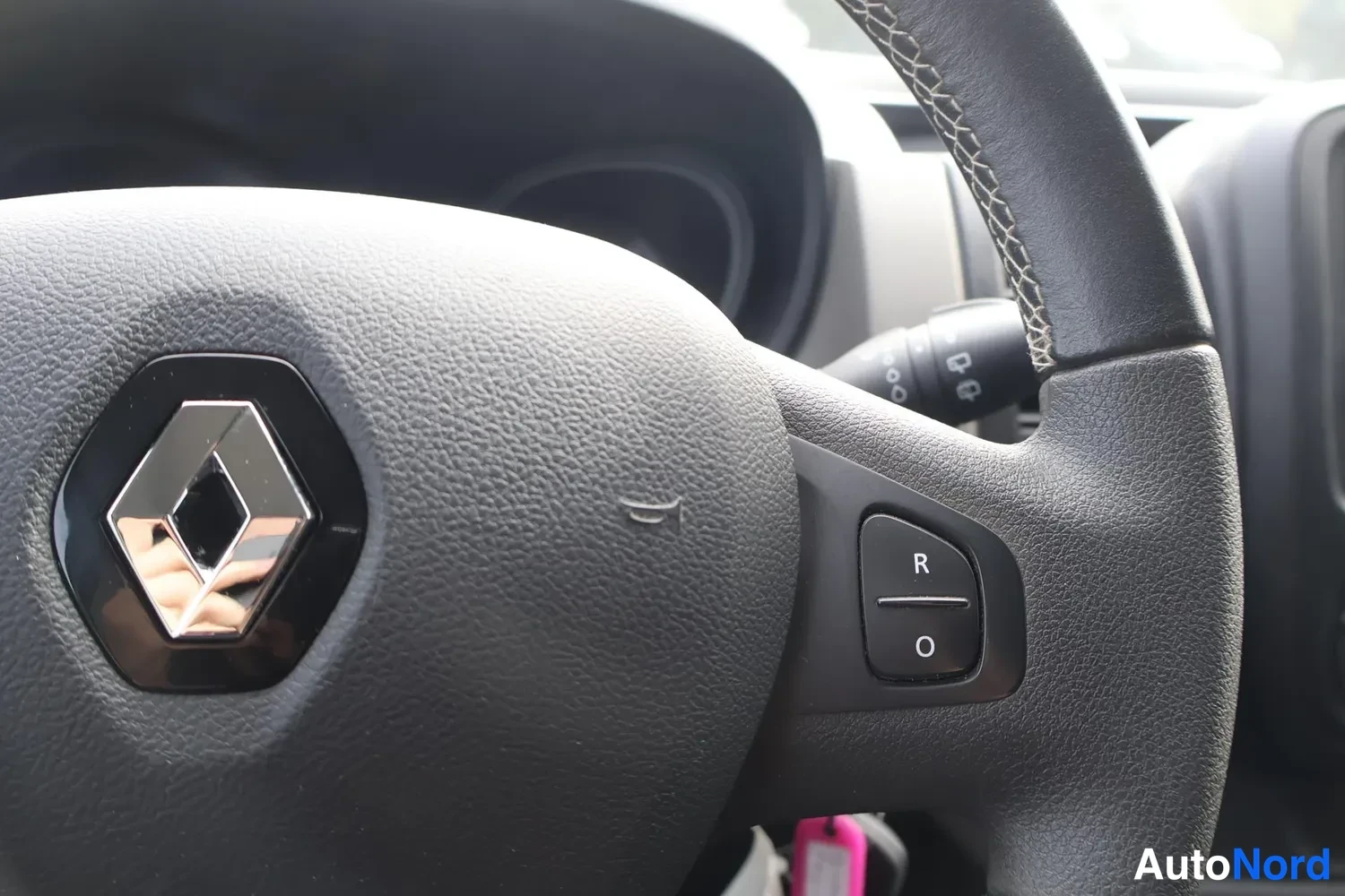 Muu: Renault-ohjauspyörän oikea puoli: R/O-painikkeet ja Renault-tunnus, avaimenperä näkyy ohjauspyörän takana.