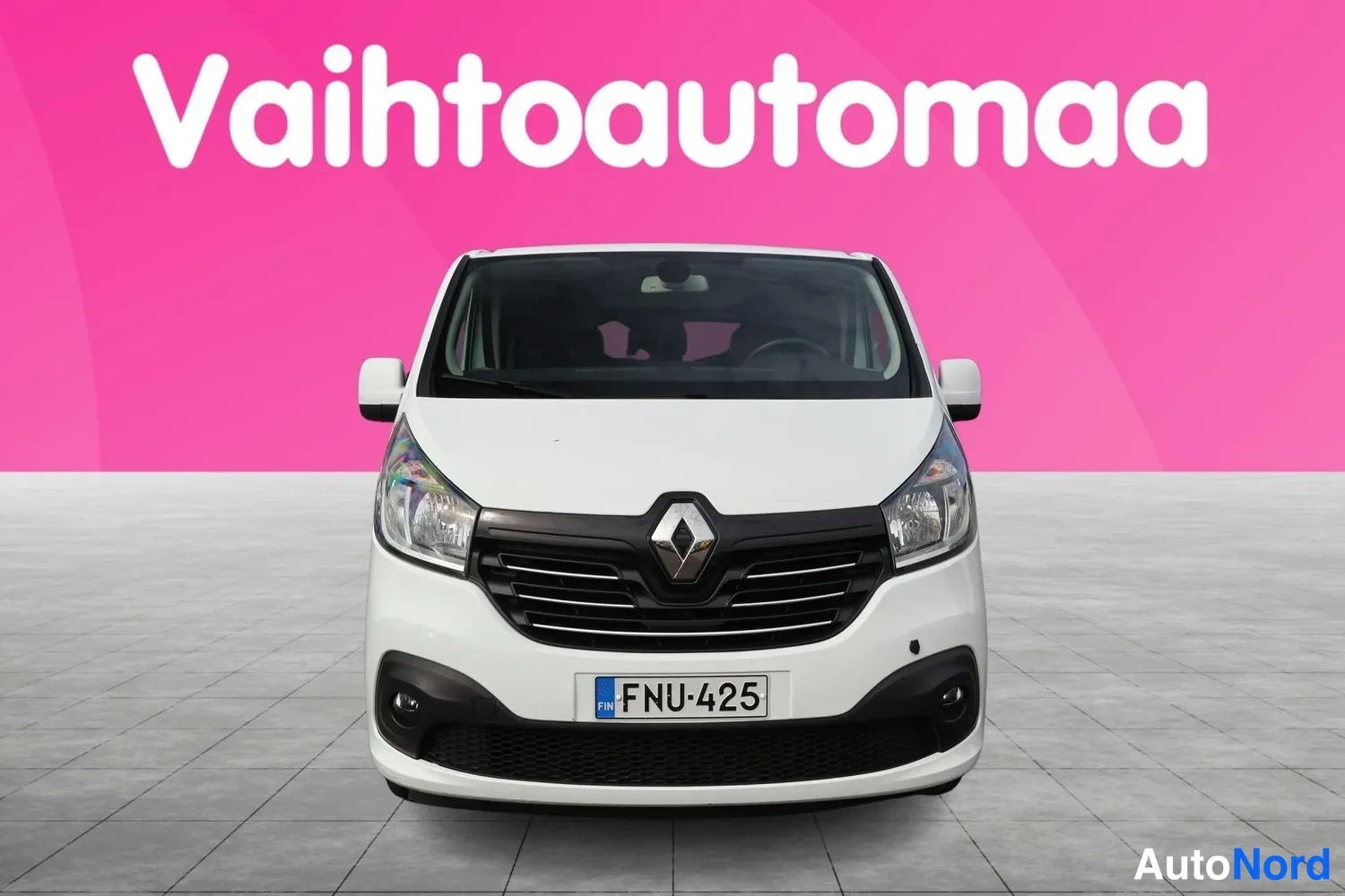 Edestä: Valkoisen Renault Trafic -pakettiauton etunäkymä suoraan edestä, rekisterikilpi, vaaleanpunainen tausta.