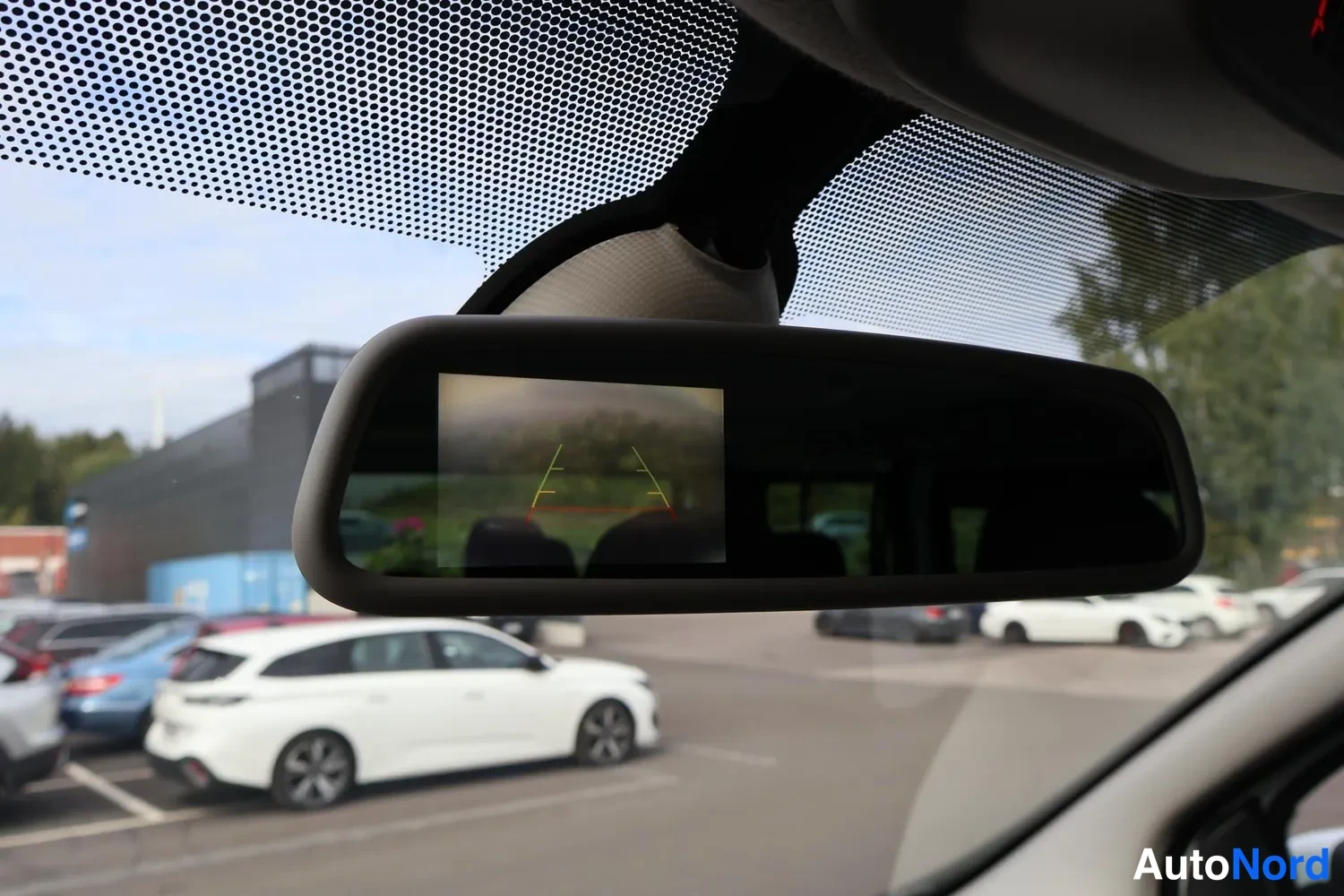 Muu: Sisäpeilin kiinnitetty näyttö, jossa näkyy peruutuskameran ruudukkolinjat; tuulilasin läpi autopaikkoja.