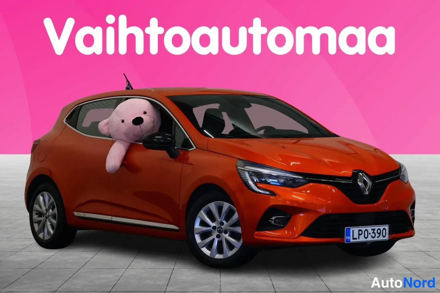 Etuviisto, nokka oikealle: Oranssi Renault Clio etu- ja sivupuoli näkyvissä, rekisteritunnus, vaaleanpunainen tausta ja Vaihtoautomaa-logoteksti.