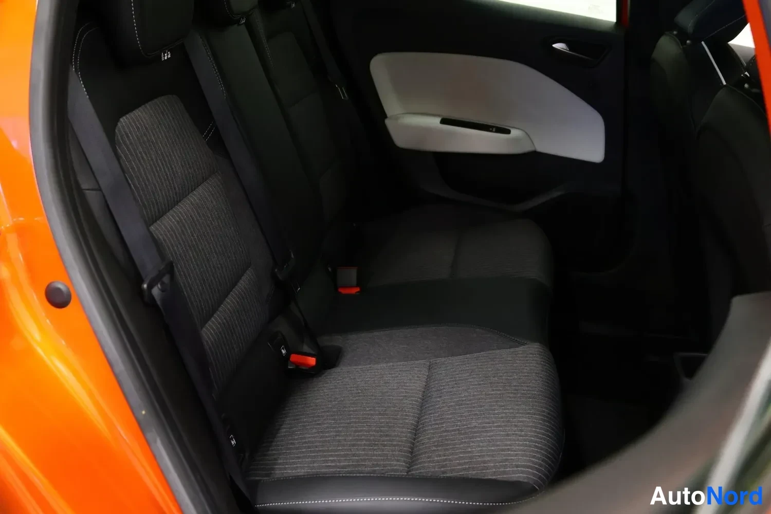Takaistuimet: Orange car's rear seat with fabric upholstery and headrests; door trim has black and light-colored inserts.