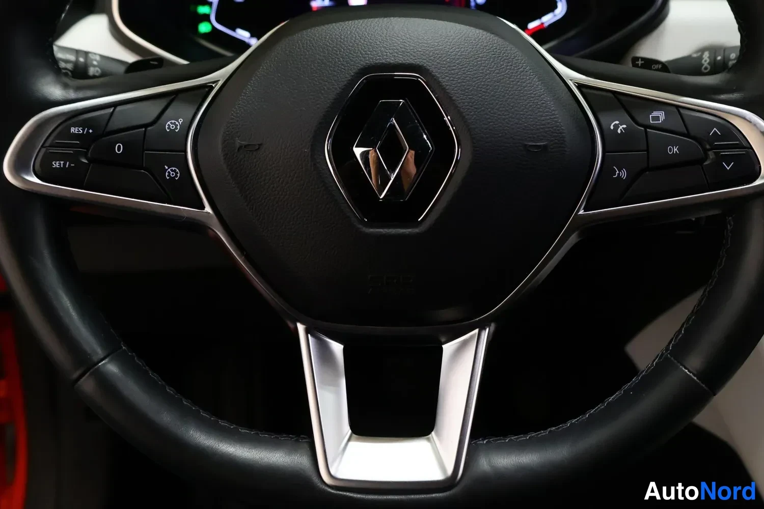 Muu: Close-up of leather-wrapped steering wheel with Renault logo; multifunction buttons on both spokes including cruise control labels RES/SET.